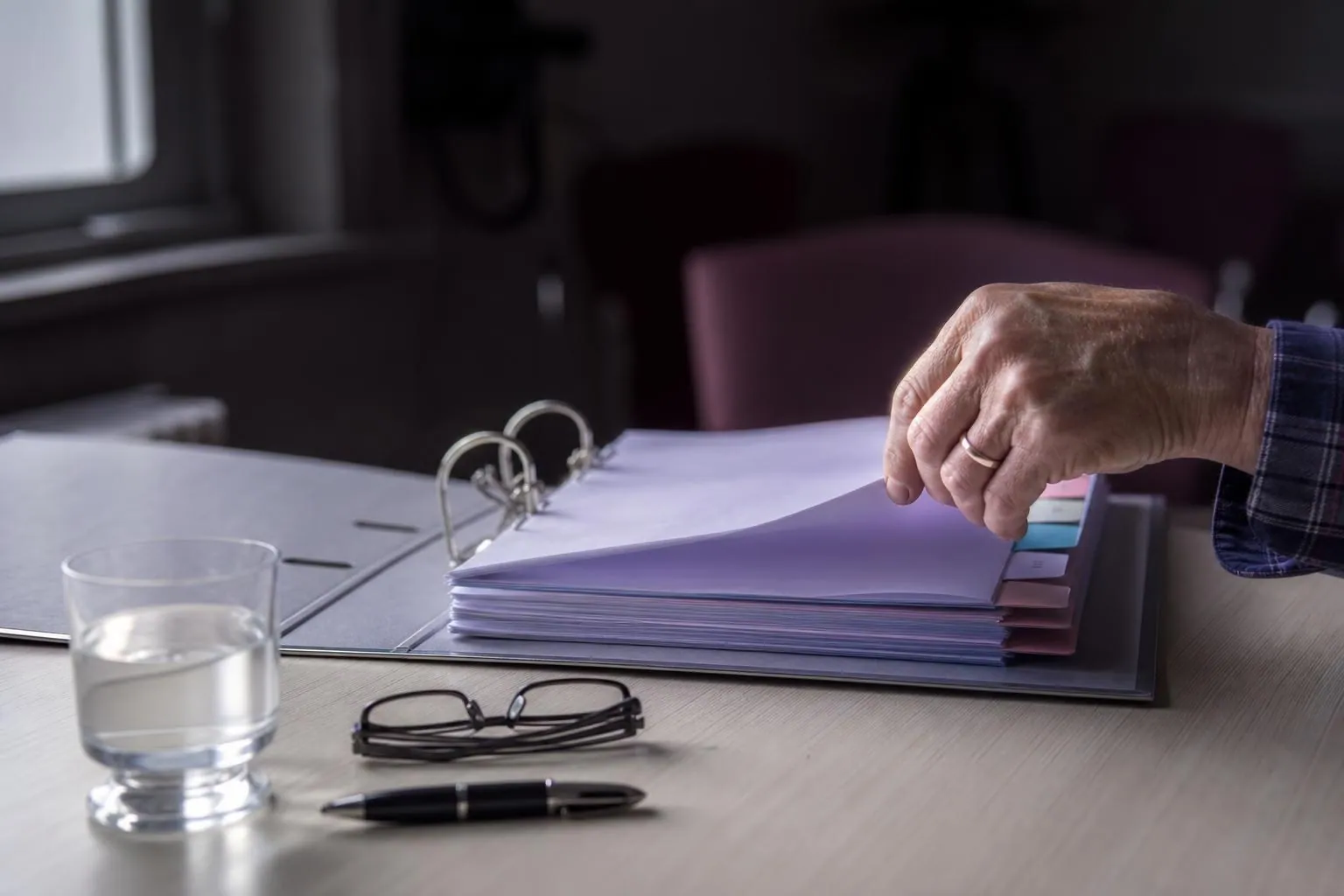 Gros plan sur un classeur à levier ouvert posé sur une table, intercalaires de couleur dépassant des pages, une main tournant un feuillet